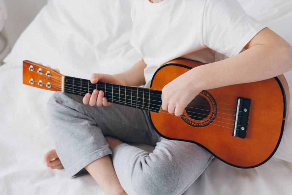 boy playing a small guitar sitting on the bed
