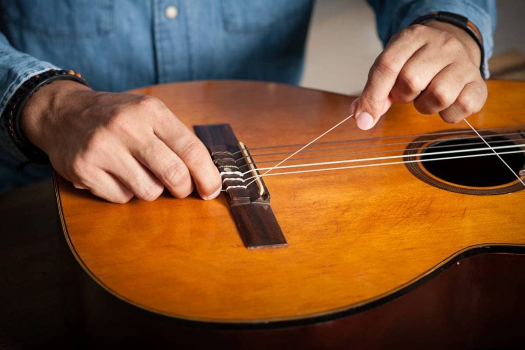 mans hand changing strings on acoustic guitar