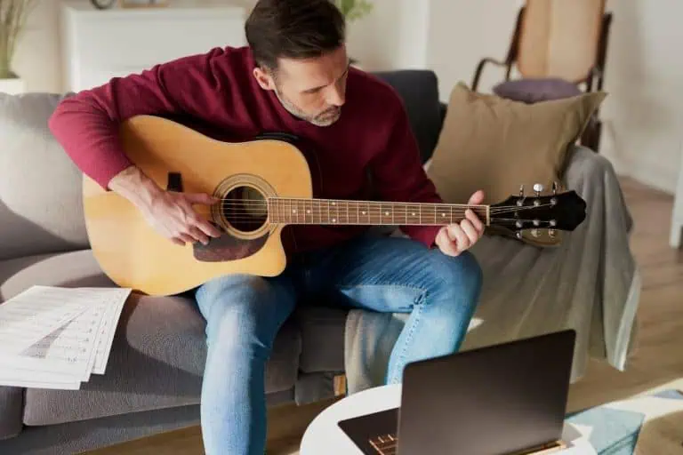 Man playing acoustic guitar on a couch, practising worship strumming patterns