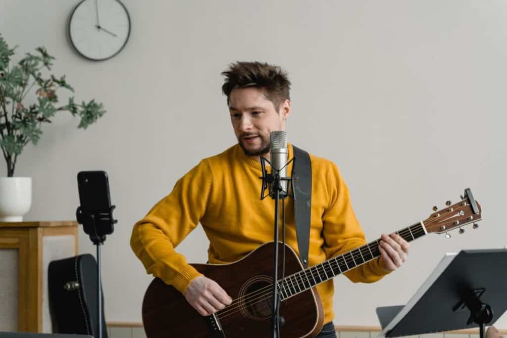 Singer-songwriter learning to record guitar and vocals at the same time at a studio microphone