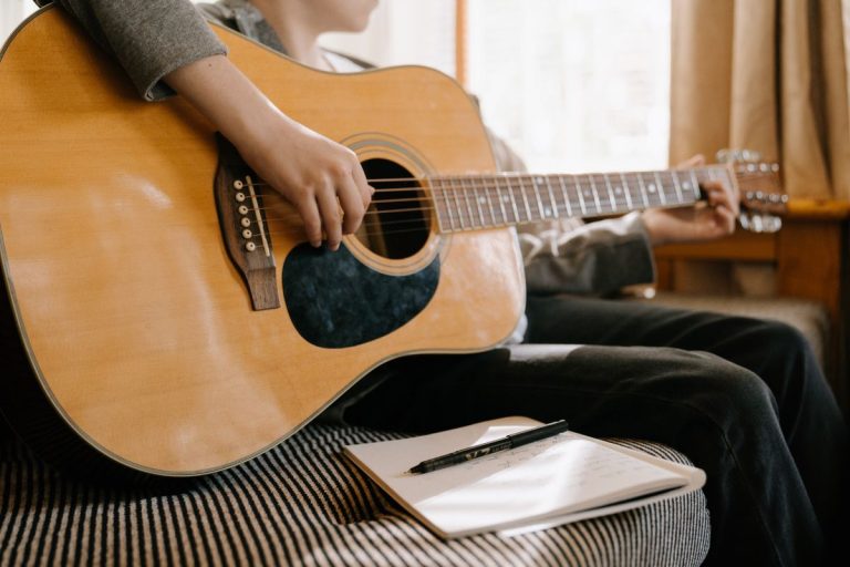 Christian songwriting prompts: songwriter with a guitar writing worship song ideas in a notebook