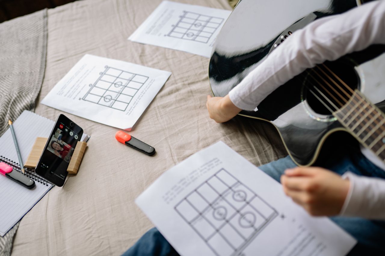 Guitarist using a phone and sheet music with a chord chart app for church practice